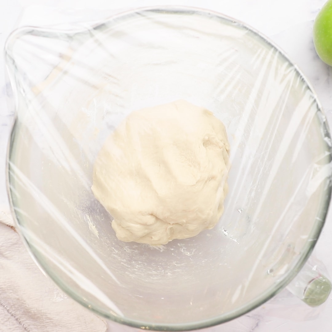 Apple Fritters dough in bowl covered with plastic wrap